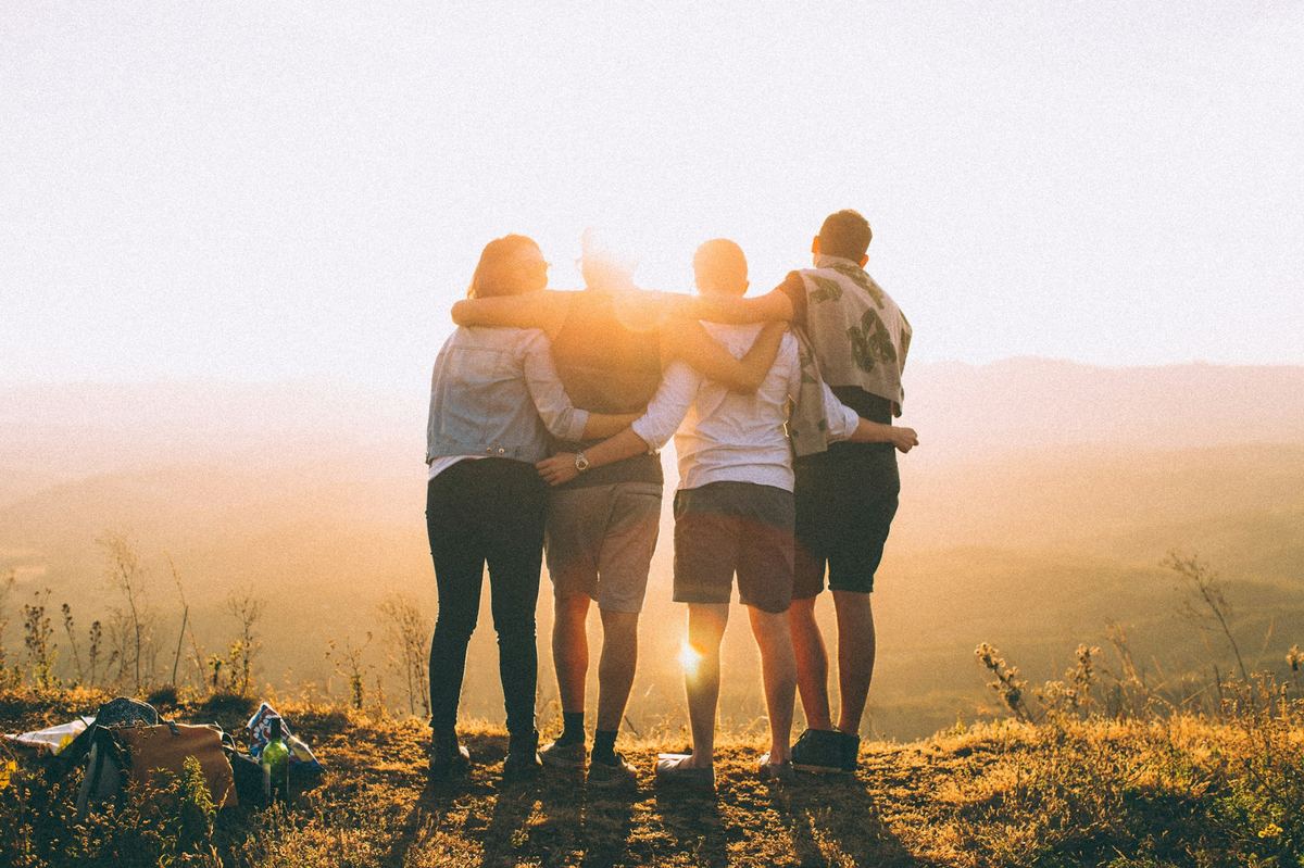 Friends with arms around each other watching the sun set together